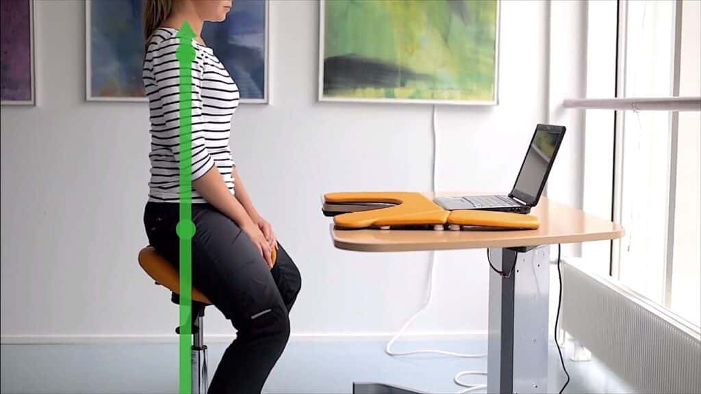 Women sitting on a saddle chair in front of a laptop working in a lightly room   